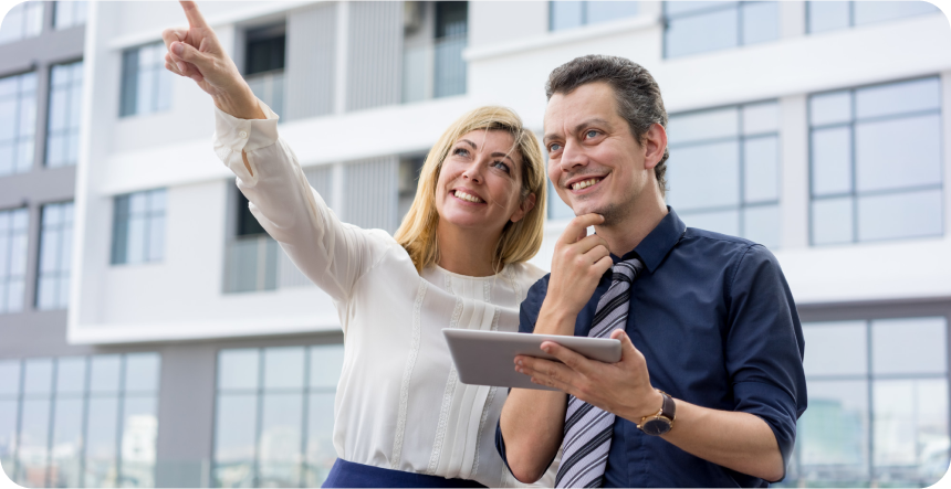 Smiling couple discussing property plans while pointing towards a building