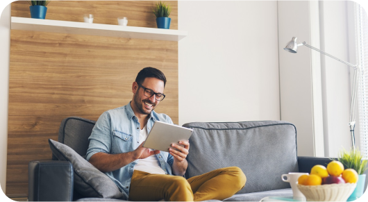 Young man sitting on a sofa reading from a digital tablet at home.
