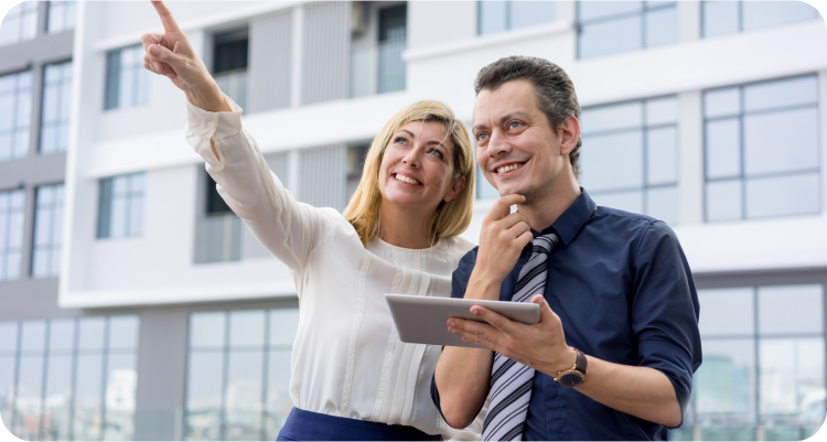 Smiling couple discussing property plans while pointing towards a building